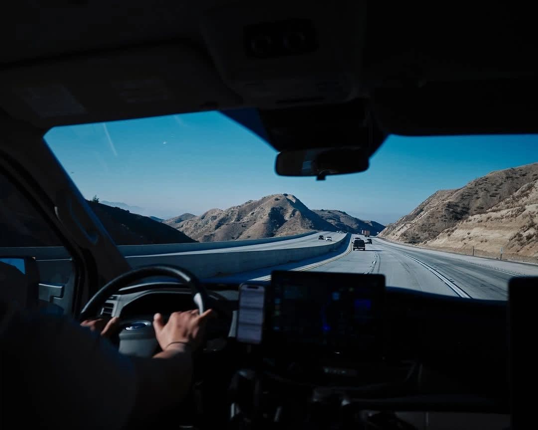 A driver at the wheel of a truck on a mountain highway, a dashboard tablet beside him.